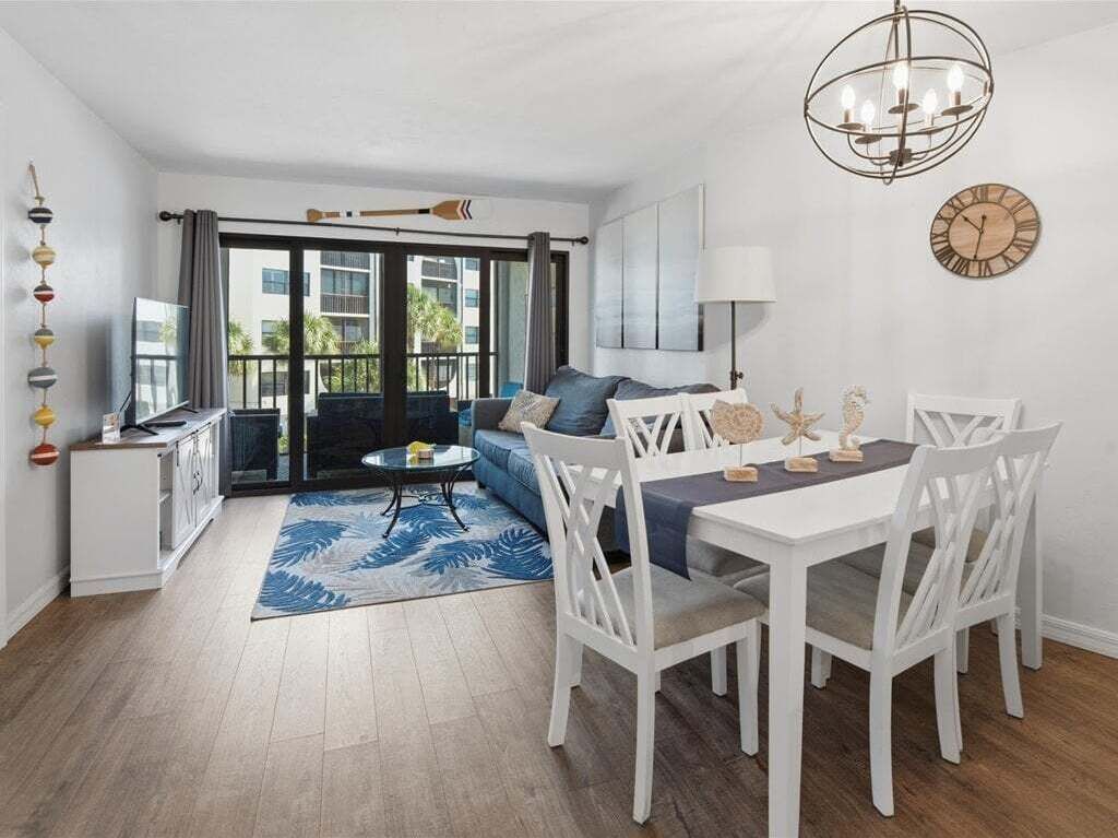 Un salon moderne comprenant un canapé, une table à manger et des chaises, un lustre, et offrant une vue à travers de grandes fenêtres.