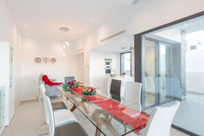Ett modernt matområde med ett glasbord, vita stolar och en röd bordslöpare.