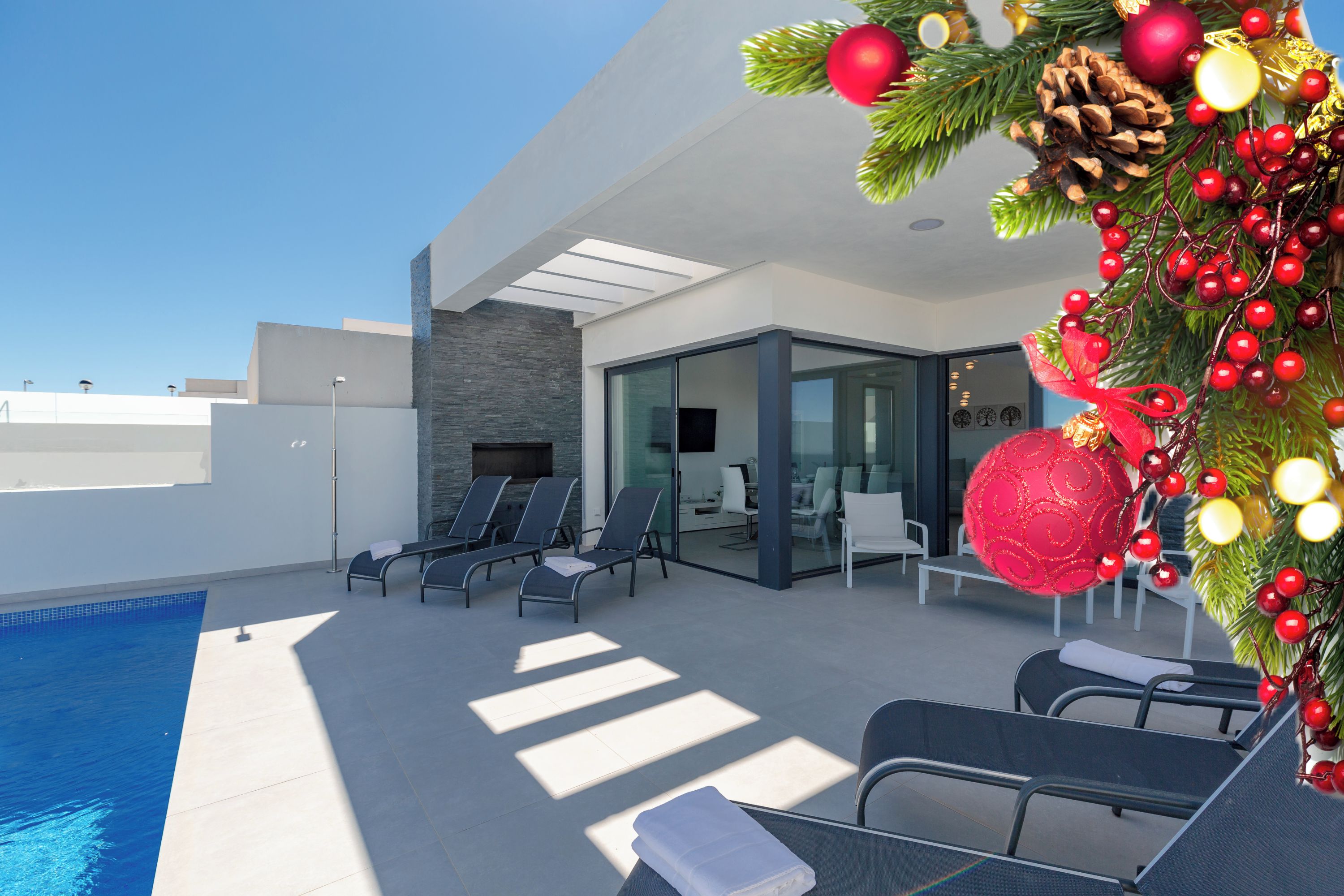 Ein moderner Poolbereich im Freien mit Liegestühlen, ein Wintergarten mit Kamin und eine Weihnachtsdeko mit roten Ornamenten.