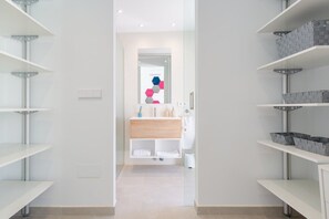 Um banheiro moderno com prateleiras brancas, toucador de madeira e espelho com decoração geométrica.