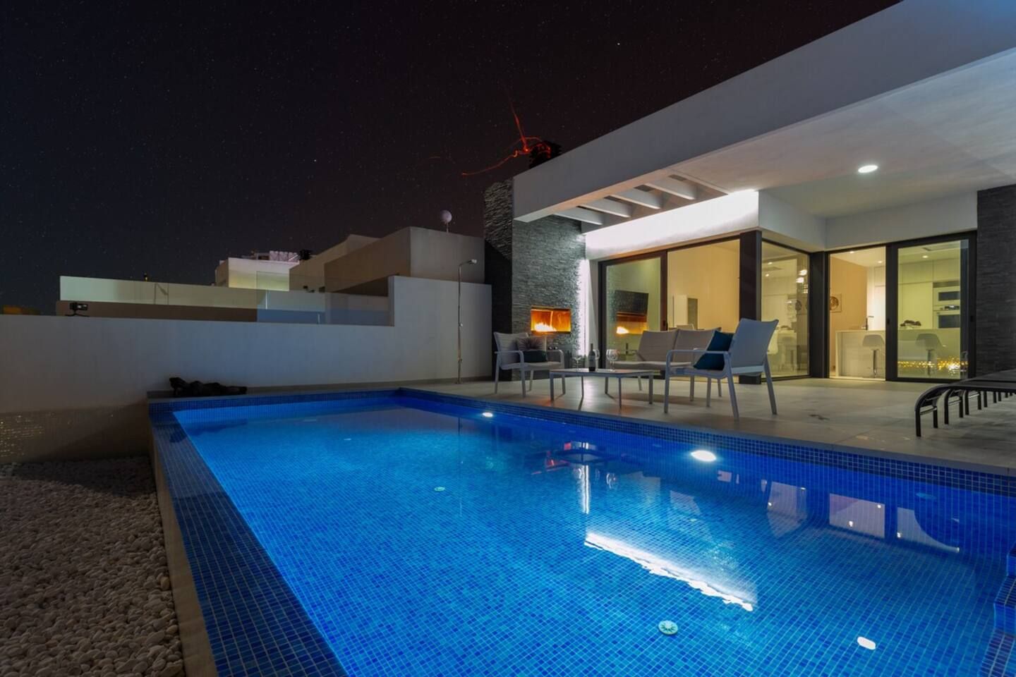 Piscina com espreguiçadeiras e uma moderna área de cozinha externa.