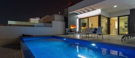 A swimming pool with lounge chairs and a modern outdoor kitchen area.