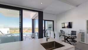Une cuisine moderne dotée d’un grand îlot central, d’un coin repas avec une table et des chaises, et d’un téléviseur fixé au mur.