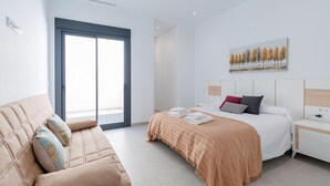 Une chambre d’hôtel moderne avec un lit, un canapé, un tableau et une vue sur l’extérieur, visible à travers une porte vitrée.