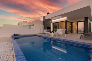 A modern outdoor swimming pool with a clear blue water surface, surrounded by white lounge chairs and a stone wall. - Fidalsa 5 Stars Sea Views (Ciudad Quesada)