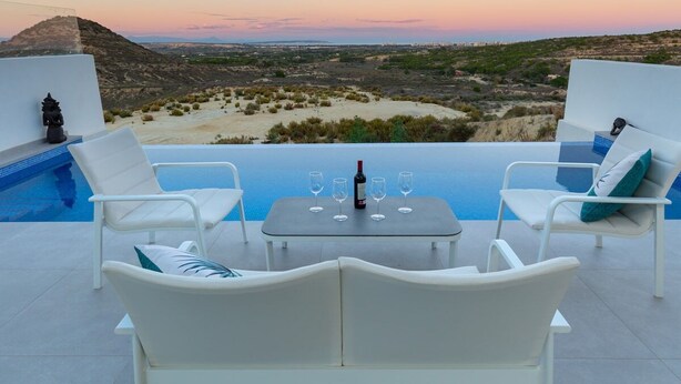 Une terrasse avec des fauteuils de jardin blancs, une table avec des verres à vin et une vue sur un paysage désertique au coucher du soleil.