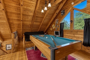 A wooden interior with a pool table, a television, and a window with a view of greenery. - Southern Serenity, Hot tub, Pool Table, Wifi, $560 FREE tickets each paid day! (Sevierville)