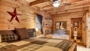 A cozy log cabin bedroom with a large bed, a ceiling fan, a star decoration, a sign reading "The Cowboy Way," and a stone wall. - Southern Serenity, Hot tub, Pool Table,  Wifi, $560 FREE tickets each paid day! (Sevierville)