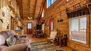 A log cabin interior with a sofa, dining table, chairs, and a fireplace. - Southern Serenity, Hot tub, Pool Table,  Wifi, $560 FREE tickets each paid day! (Sevierville)