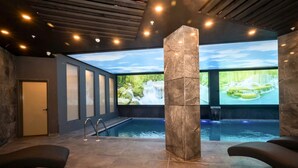 Ein Wellnessbereich mit Pool, Sitzgelegenheiten und einer großen Wand, die eine Wasserfallszene zeigt.