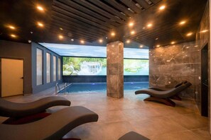 A spa room with a large window, a pool, and two massage chairs.