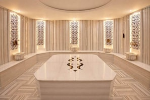 A spacious room with a large marble table, flanked by tall, patterned walls and small, round tables.