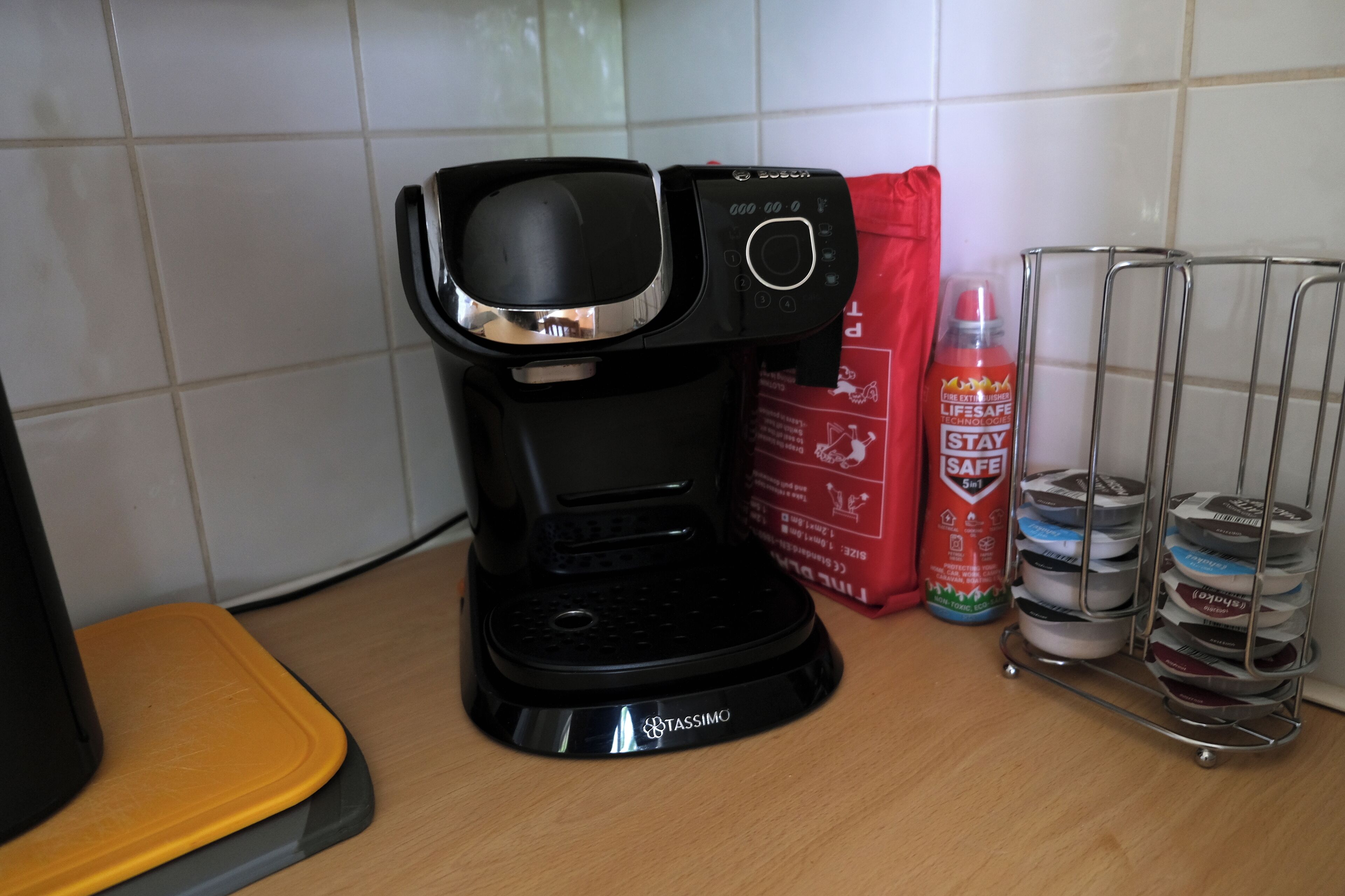 A coffee maker on a kitchen counter with a red canister and a metal rack with containers.