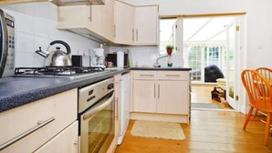 A kitchen with white cabinets, a gas stove, and a sink. - Quite Garden Flat with parking (London)