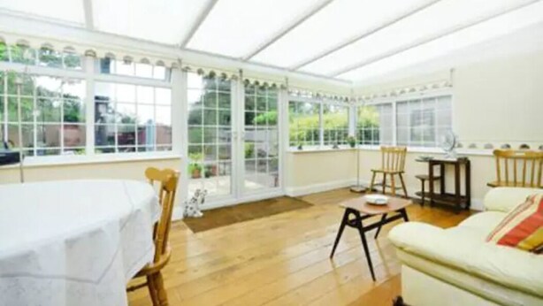 A conservatory with a table and chairs, a sofa, and a view of greenery outside. - Quite Garden Flat with parking (London)