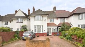 A row of two-story houses with a paved driveway and a parked car. - Quite Garden Flat with parking (London)