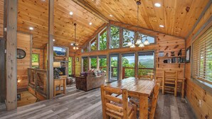 Una cabaña de madera espaciosa con una gran mesa de comedor, varios ventanales y una chimenea.