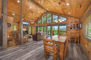 Une cabane en bois spacieuse, dotée d’une grande table à manger, de nombreuses fenêtres et d’une cheminée.