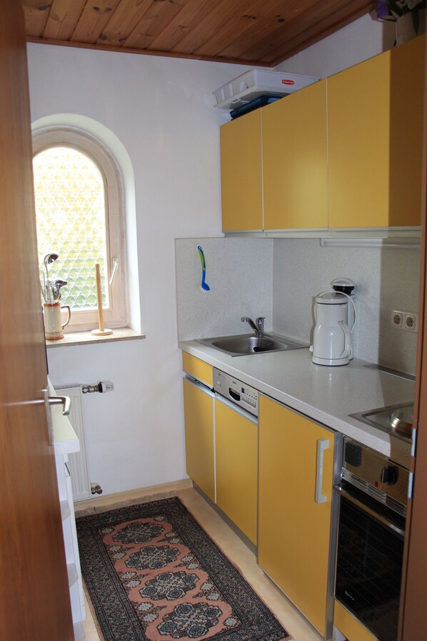 A compact kitchen with yellow cabinets, a white countertop, a coffee maker, and a window with a view.