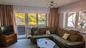A living room with a sectional sofa, a flat-screen TV on a wooden cabinet, and a large window with curtains.