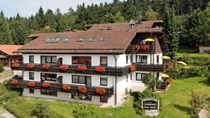 A multi-story hotel with balconies adorned with red flowers, a garden area, and a sign indicating a restaurant.