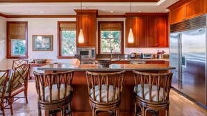 A modern kitchen with wooden cabinets, a stainless steel refrigerator, and a central island with bar stools.