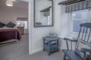 A bedroom with a bed, a nightstand, a chair, a window, and a mirror.