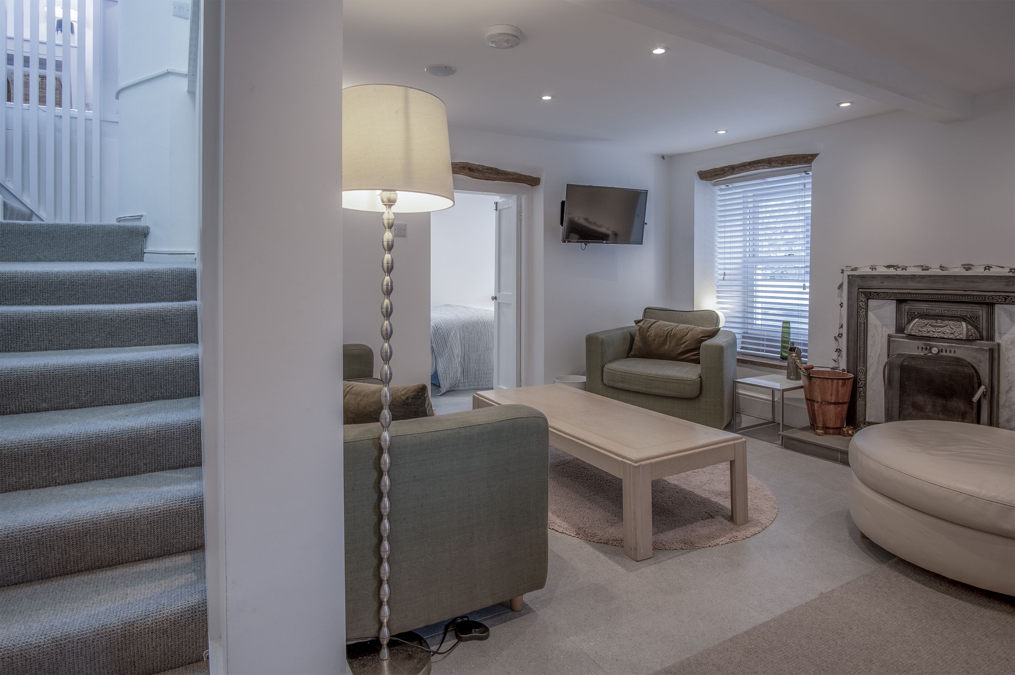 A modern living room with a staircase, a flat-screen TV, a fireplace, and a sofa.