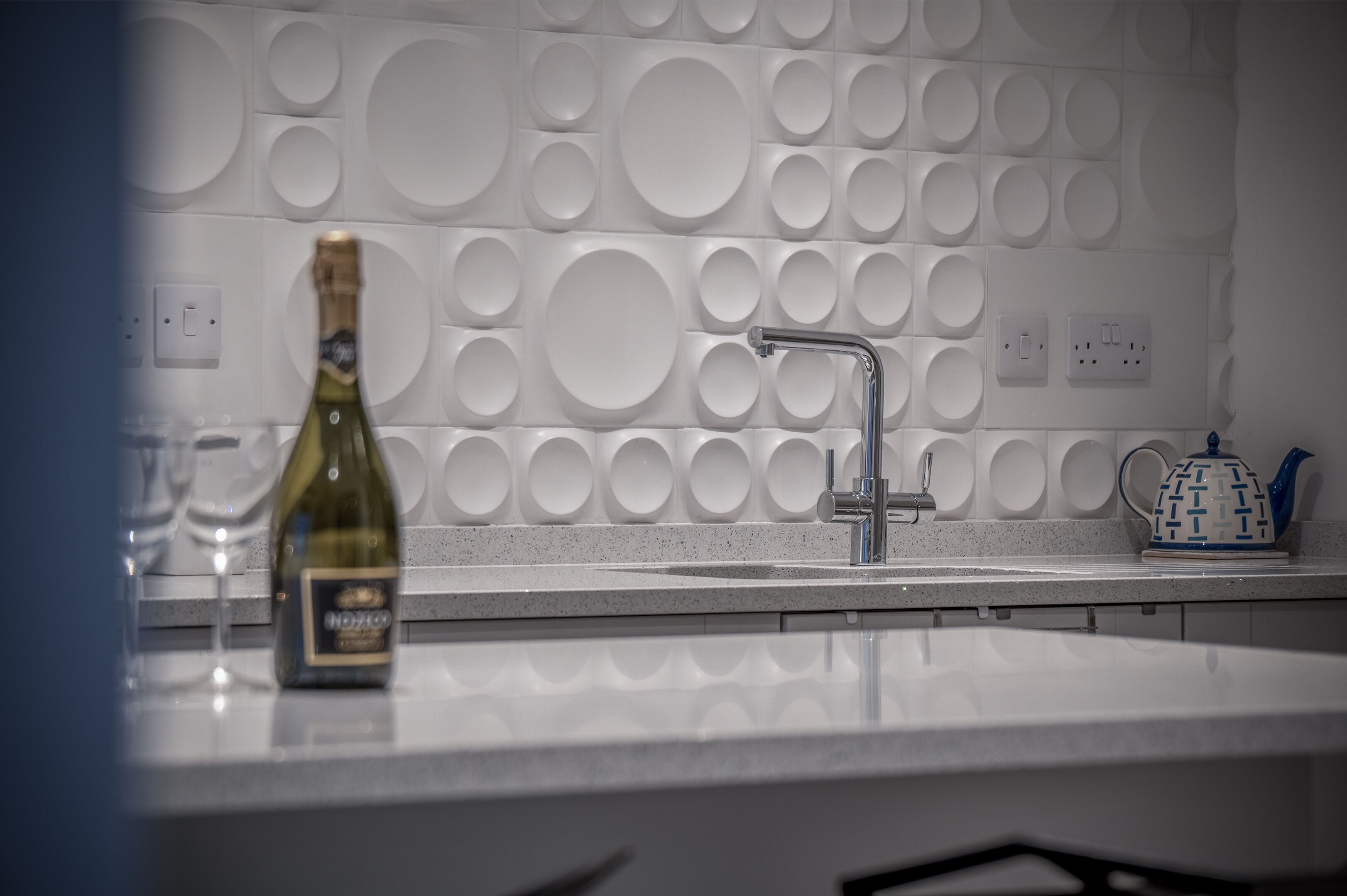 A modern kitchen with a white countertop, a wine bottle, and a kettle.