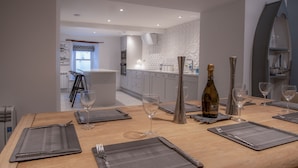 Un espace de salle à manger moderne avec une table en bois dressée pour six personnes, comprenant des verres à vin et une bouteille de champagne.