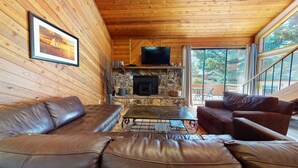 Un intérieur de chalet chaleureux avec une cheminée en pierre, des canapés en cuir et un téléviseur.