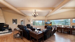 A cozy living room with a fireplace, leather sofas, a chandelier, and a large window offering a scenic view. - Three Pet Friendly cabins on 3.5 Acres -  Hot Tub/Views - 14 minutes to Purg (Durango)
