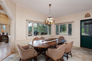 A dining area with a large wooden table and six upholstered chairs. There are large windows providing a view of the outdoors. - Three Pet Friendly cabins on 3.5 Acres - Hot Tub/Views - 14 minutes to Purg (Durango)