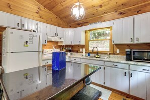 A modern kitchen with white cabinets, a granite countertop, a built-in microwave, and a large window.