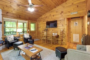 A cozy cabin interior with wooden walls, a ceiling fan, a TV mounted on the wall, and a sign indicating a steep slope.
