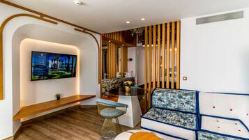 Una sala de estar moderna con un televisor montado en la pared, un banco de madera, una mesa de centro de vidrio y un sofá estampado.