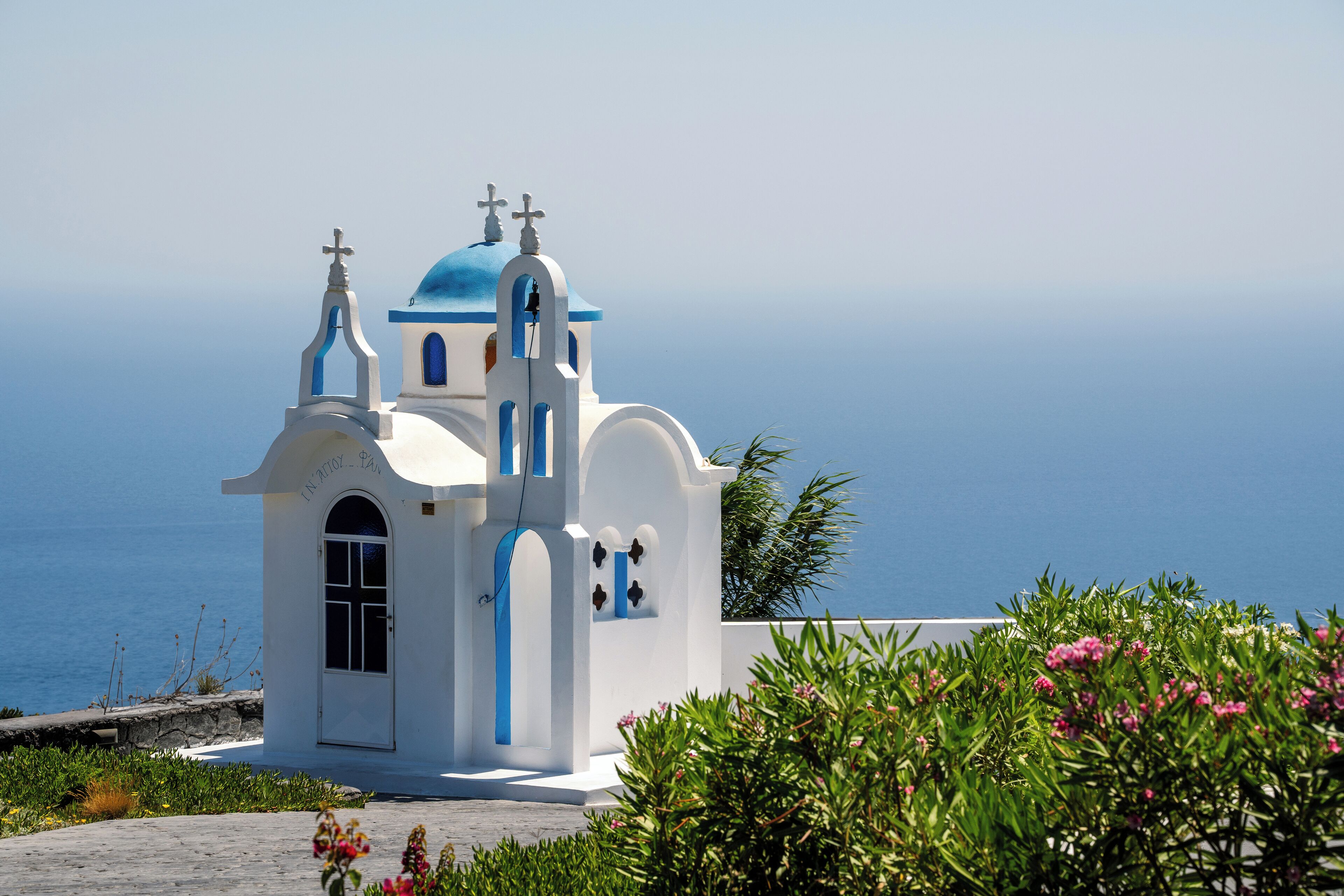 A white church with blue accents and a cross on top, located near a body of water.