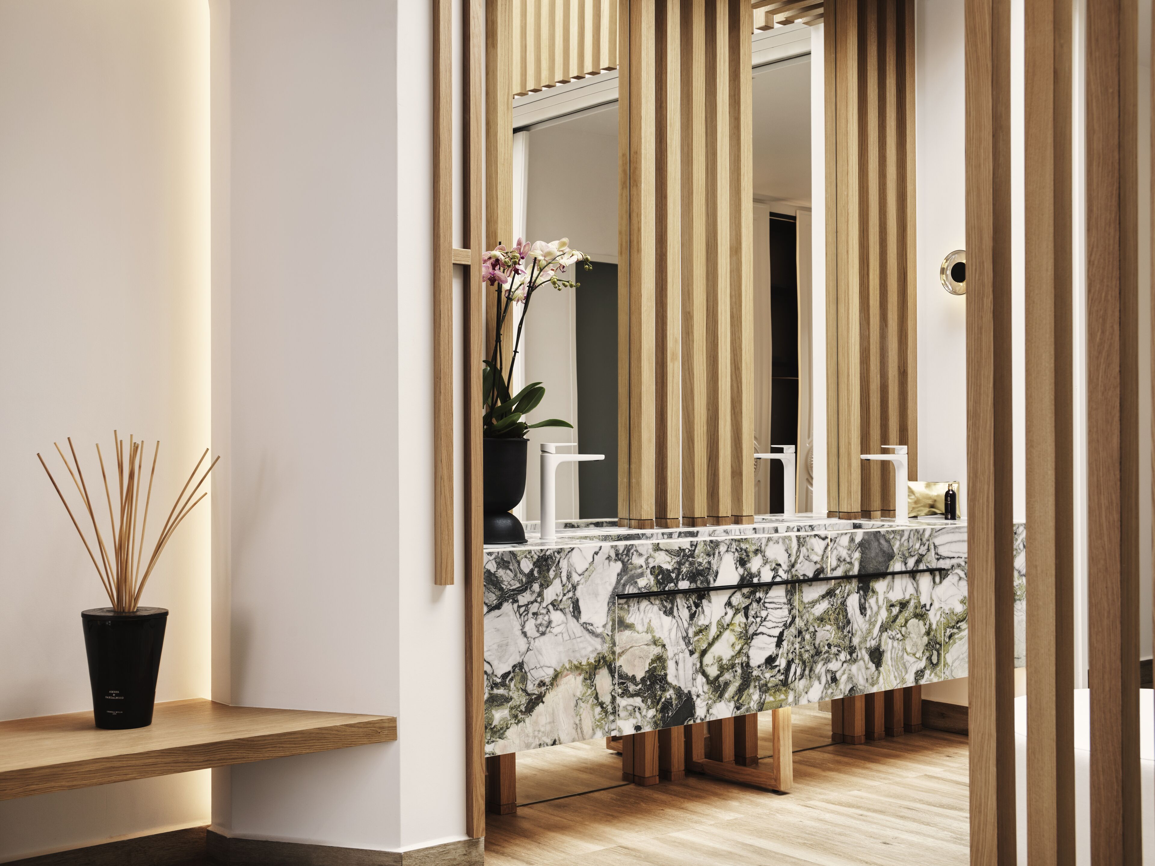 Un baño moderno con tocador de mármol, paneles de madera y una orquídea en maceta.