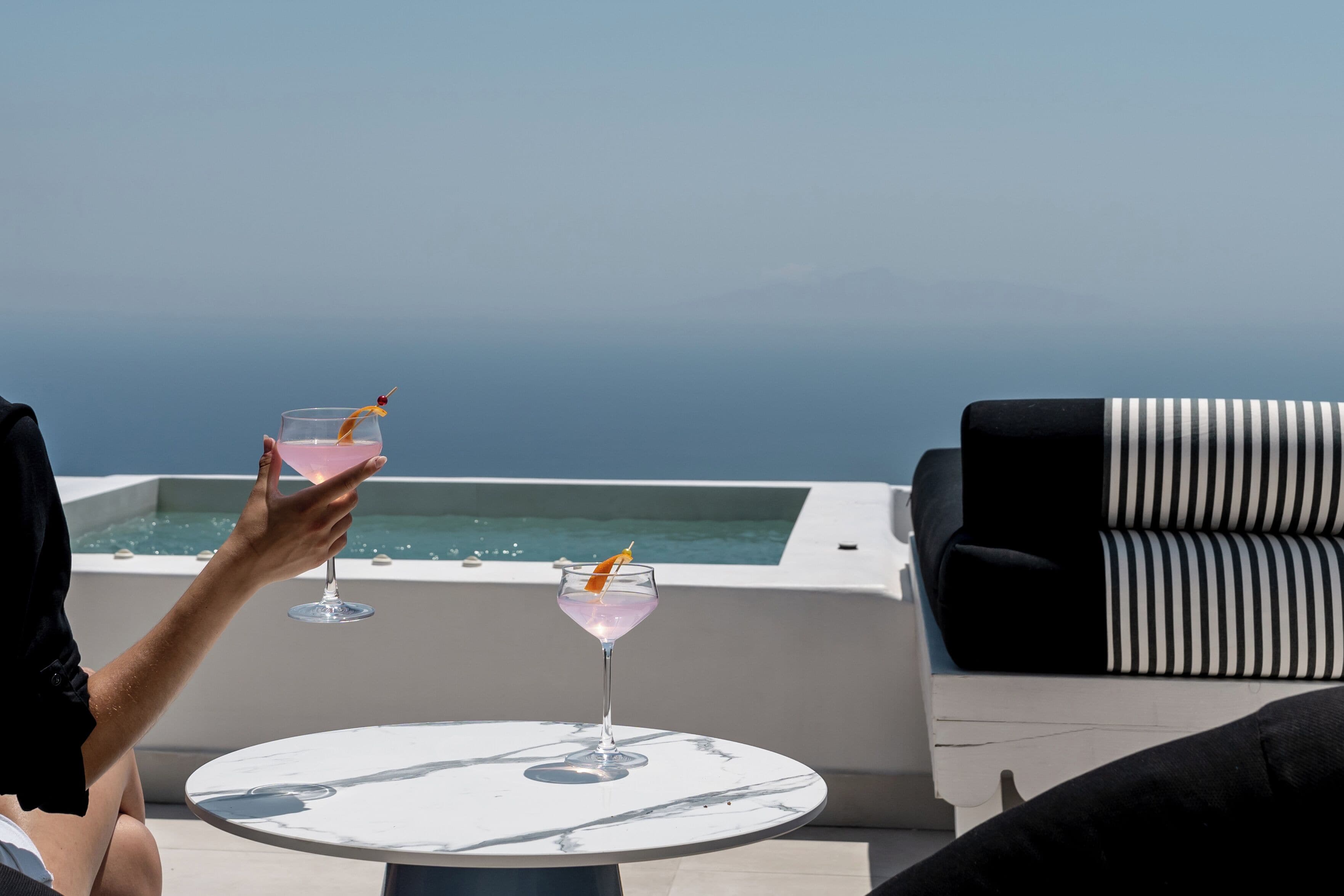 A person holding a drink at a table with a view of the ocean.