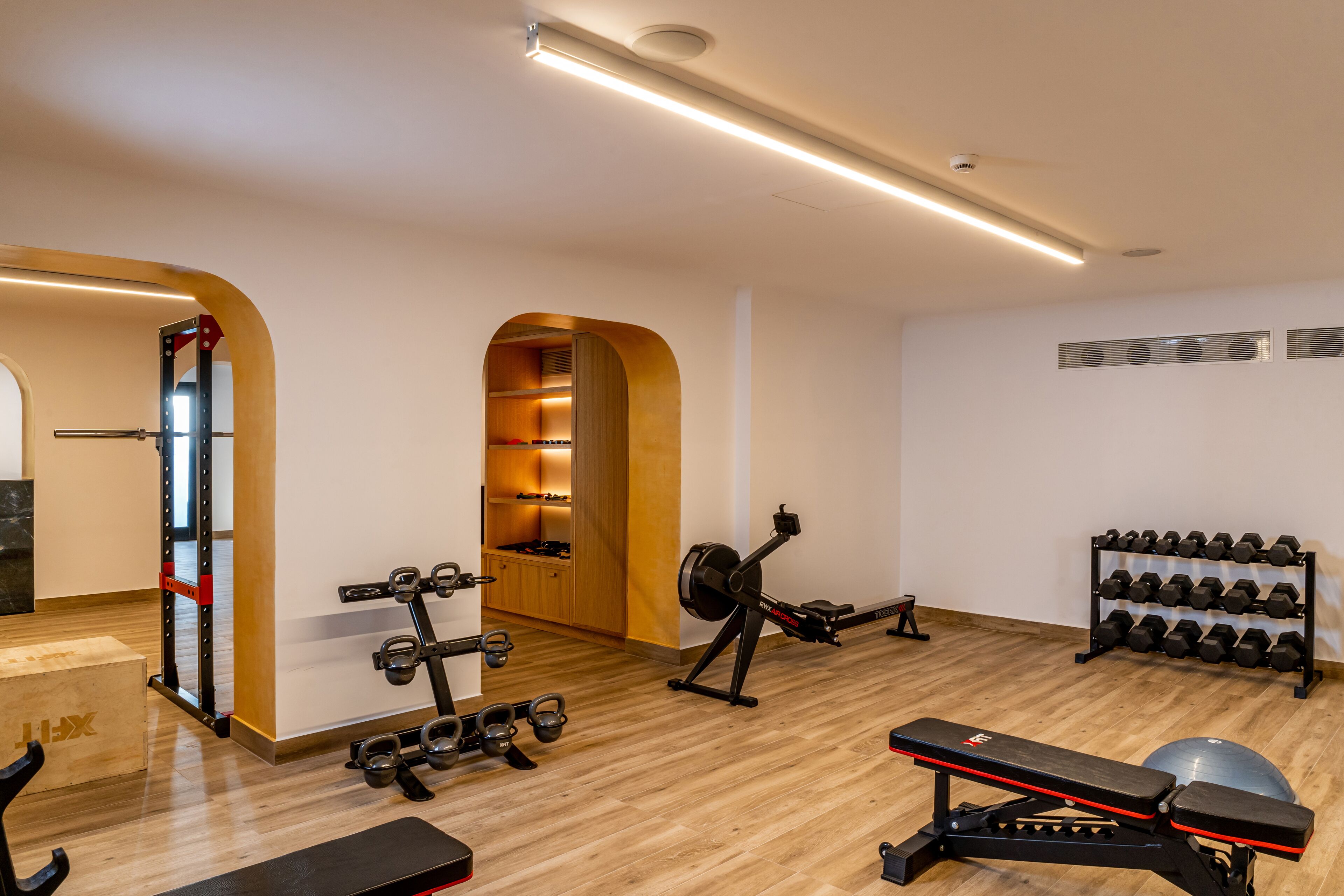 A gym with exercise equipment, a squat rack, a bench, and a rack of dumbbells.
