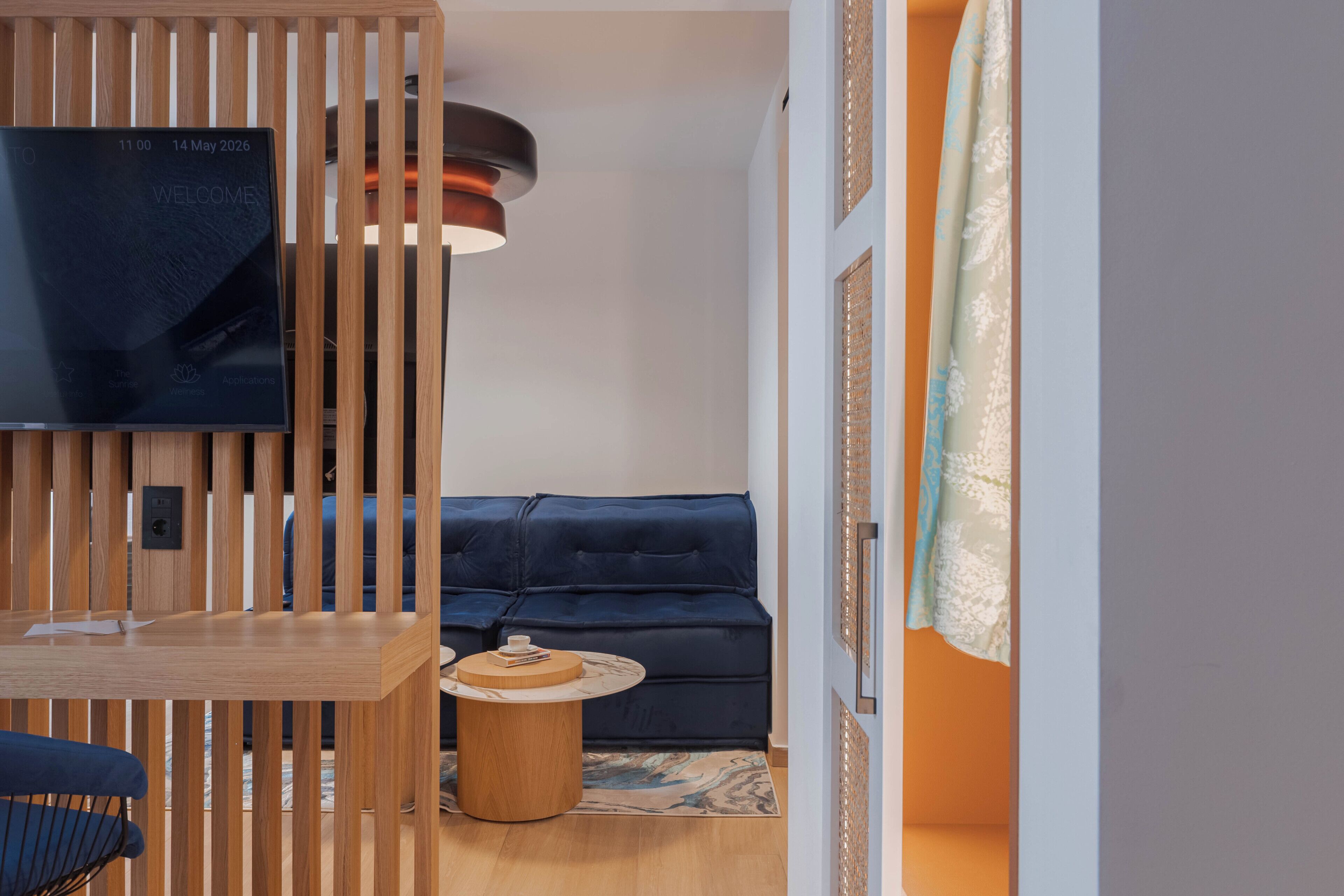 A modern living room with a dark blue sofa, a wooden TV stand, a round wooden side table, and a ceiling light fixture.