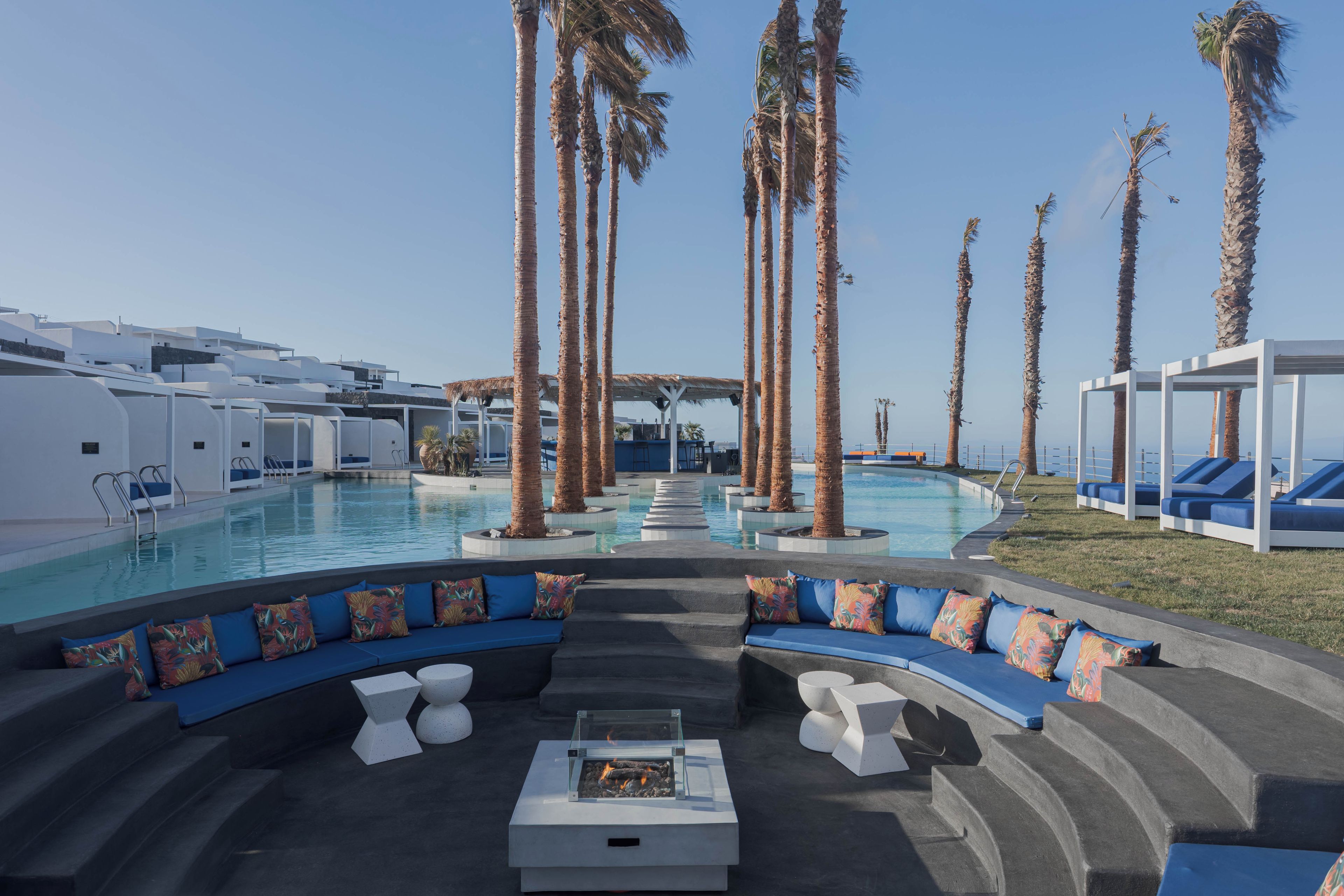 A pool area with a curved seating area, palm trees, and a clear sky.