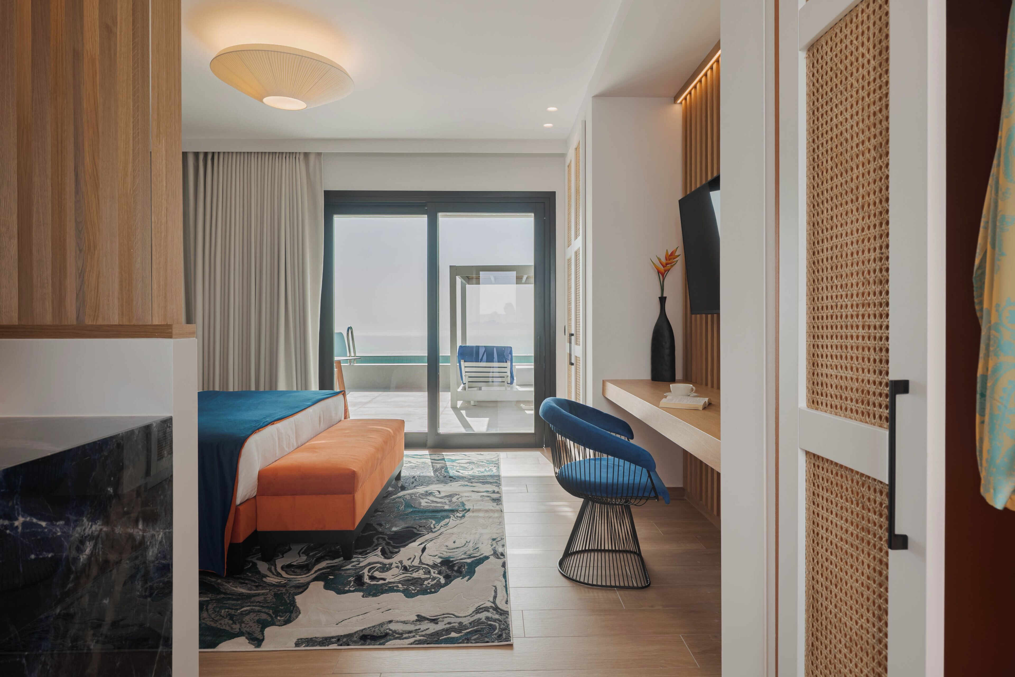 A modern hotel room with a bed, a seating area, a television, and a balcony with a view.