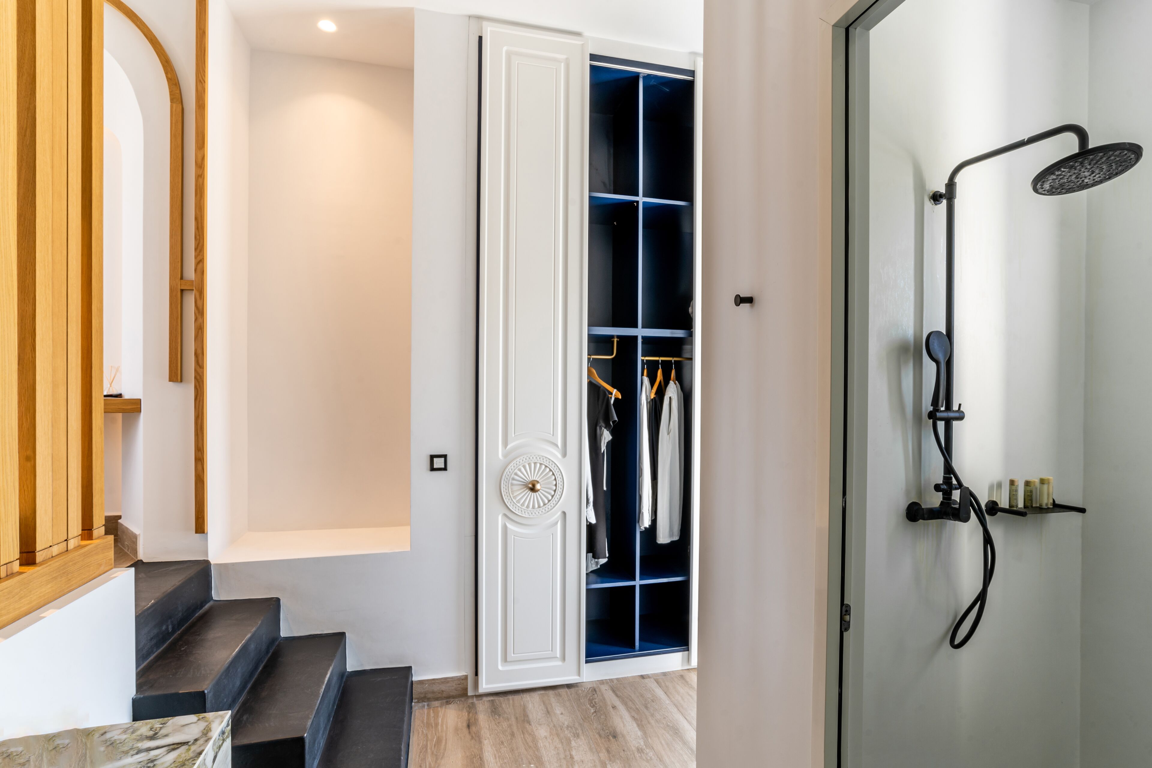 A modern bathroom with a shower, a walk-in closet with clothes, and a wooden staircase.