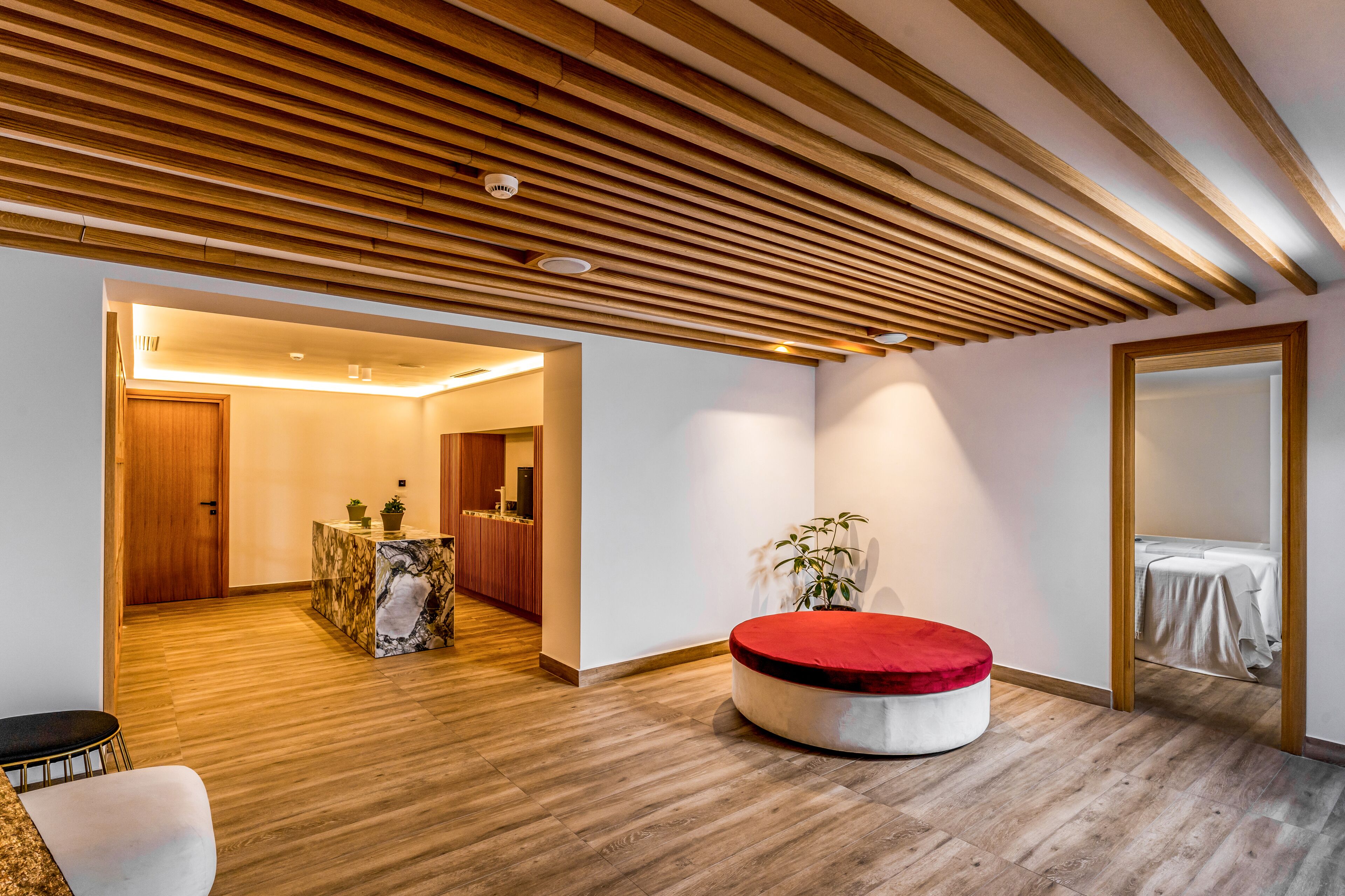 A modern interior with a wooden ceiling, a round red ottoman, and a marble coffee table.