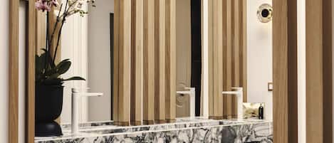 A modern bathroom with a marble countertop, wooden accents, and a potted orchid.