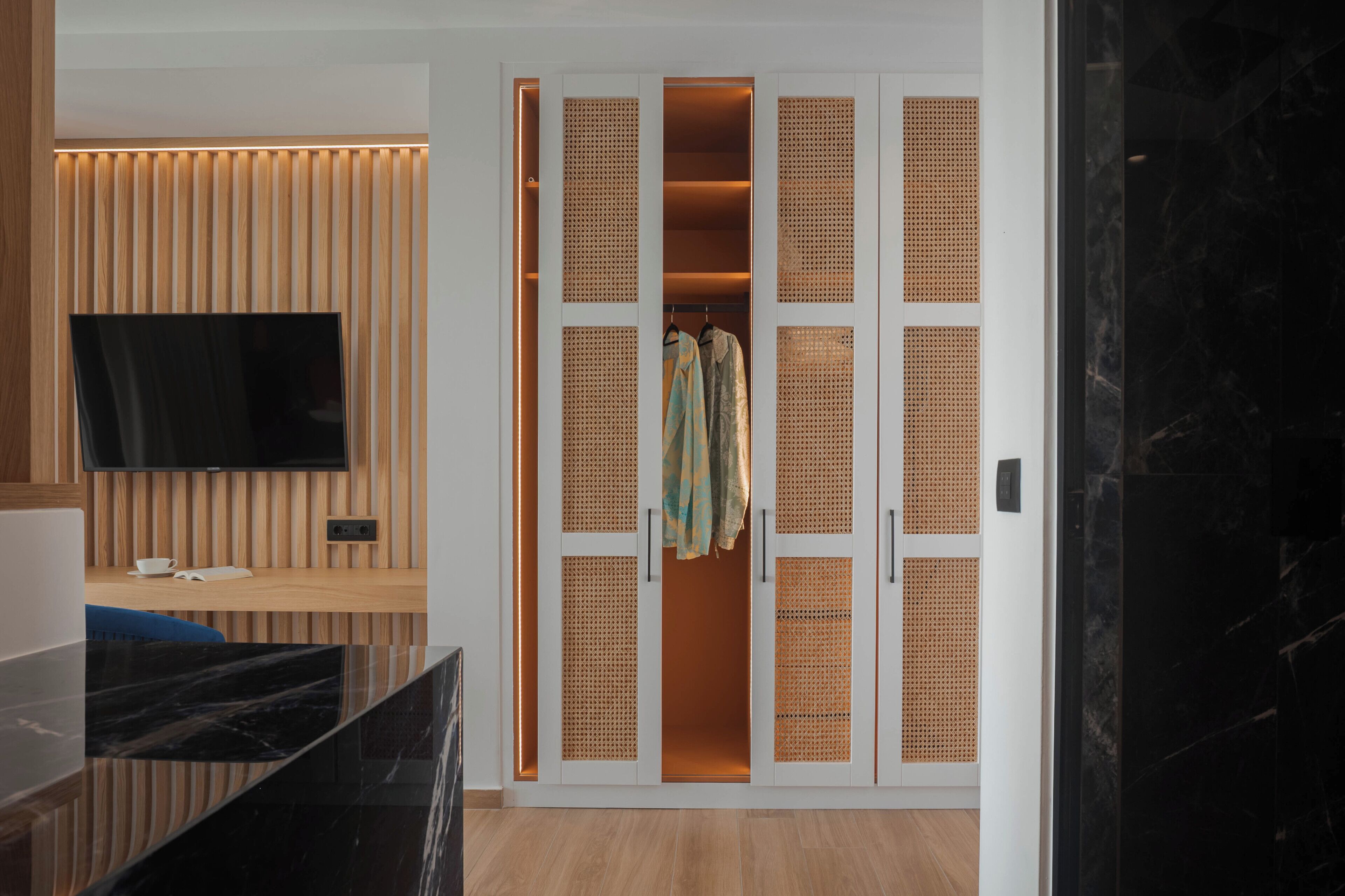 Une chambre moderne avec un mur recouvert de panneaux en bois, un téléviseur à écran plat, un comptoir en marbre noir et un dressing avec des cloisons en osier.