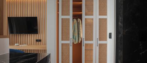A modern room with a wooden panel wall, a flat-screen TV, a black marble countertop, and a walk-in closet with woven partitions.