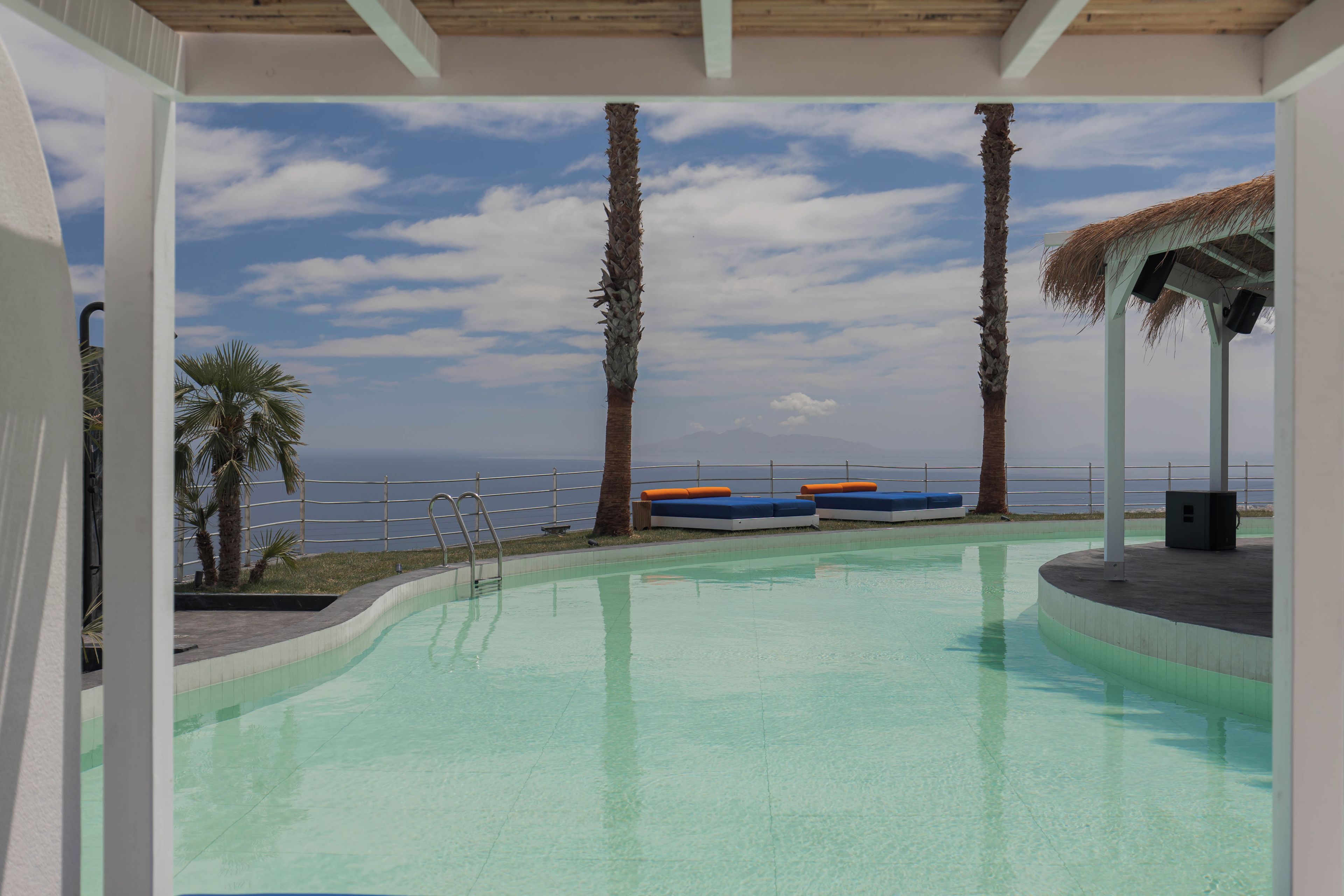 Una piscina con sillones de descanso, palmeras y vistas al mar.