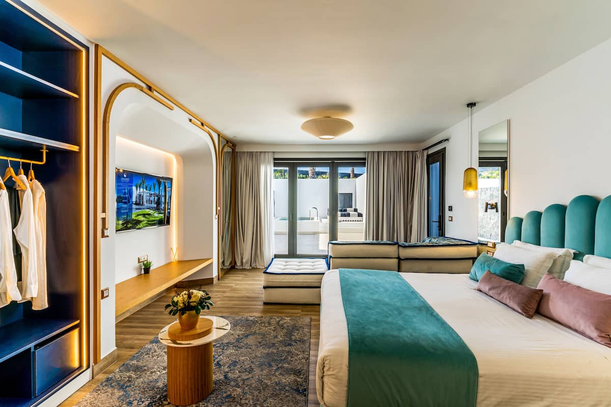 Ein modernes Hotelzimmer mit einem großen Bett, einer Sitzecke, einem Fernseher und Blick ins Freie.